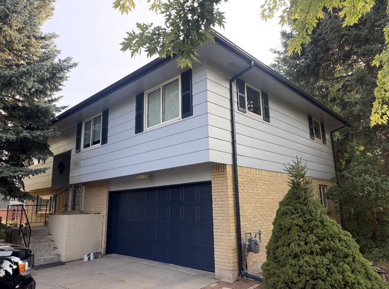 Bi-level home in light blue siding with navy garage door, shutters and gutters