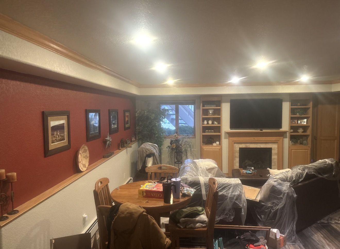 Basement with a deep red accent wall, furniture wrapped in plastic during painting